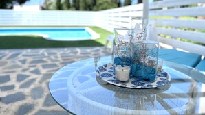 A glass table with a white and blue patterned tablecloth, a candle, and decorative glassware with blue and white elements. - STAY ALKYONI Villa (Protaras)