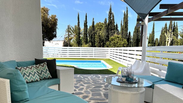A patio area with wicker furniture, a glass table, and a view of a swimming pool. - STAY ALKYONI Villa (Protaras)