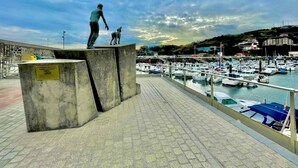 A waterfront promenade with a statue of a man and a dog, a marina with boats, and a hilly landscape in the background. - Katorse, 2 bedrooms, 2 bathrooms and elevator (Bermeo)