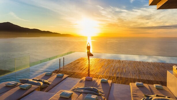 Vista del atardecer desde una terraza de madera con sillones de descanso y un tapete de yoga.