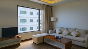Habitación de hotel con un ventanal grande, un televisor de pantalla plana, un sofá, una mesita de café y una lámpara.