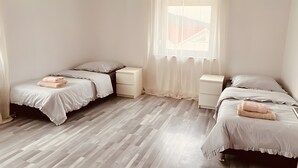 Een slaapkamer met twee bedden, een raam met dunne gordijnen en een houten vloer.
