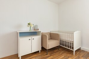 A white crib with a white mattress, a beige chair, and a white cabinet with a blue shelf.