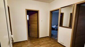 Een gang met houten vloeren, een deur naar een kamer met een bed en een spiegel aan de muur.