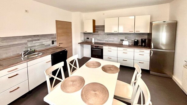 Een moderne keuken met witte kasten, een roestvrijstalen koelkast en een eettafel met vier stoelen.