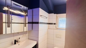 Een moderne badkamer met een wit wastafelmeubel, donkere kastjes, een toilet en een raam met uitzicht.