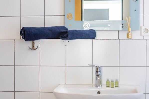 Un baño con un lavamanos blanco, un espejo con un marco decorativo y un perchero con una toalla azul.