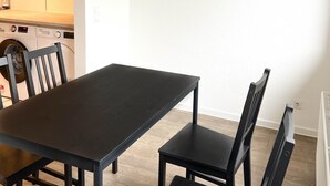 Un comedor con mesa y sillas, un cuadro con motivos de café, y una lavadora al fondo.