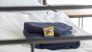 Una cama bien hecha con una toalla azul doblada y un paquete de Haribo Goldbären sobre la almohada.