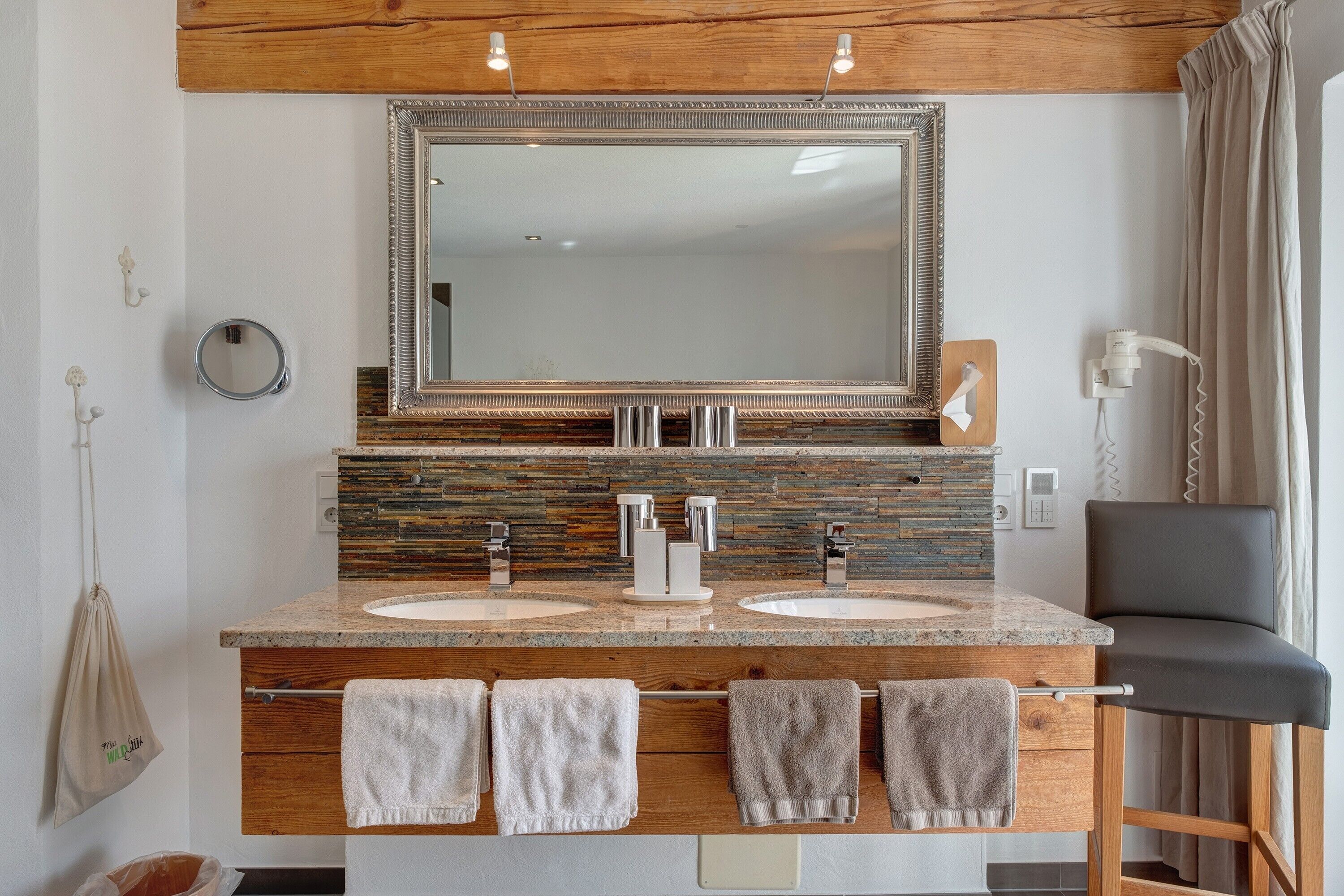 Une salle de bain avec deux lavabos, un grand miroir, un meuble-lavabo en bois et une chaise.