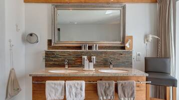 Une salle de bain avec deux lavabos, un grand miroir, un meuble-lavabo en bois et une chaise.