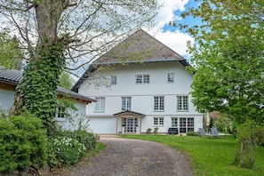 A two-story house with a white exterior, a tiled roof, and a gravel driveway leading to a front door.
