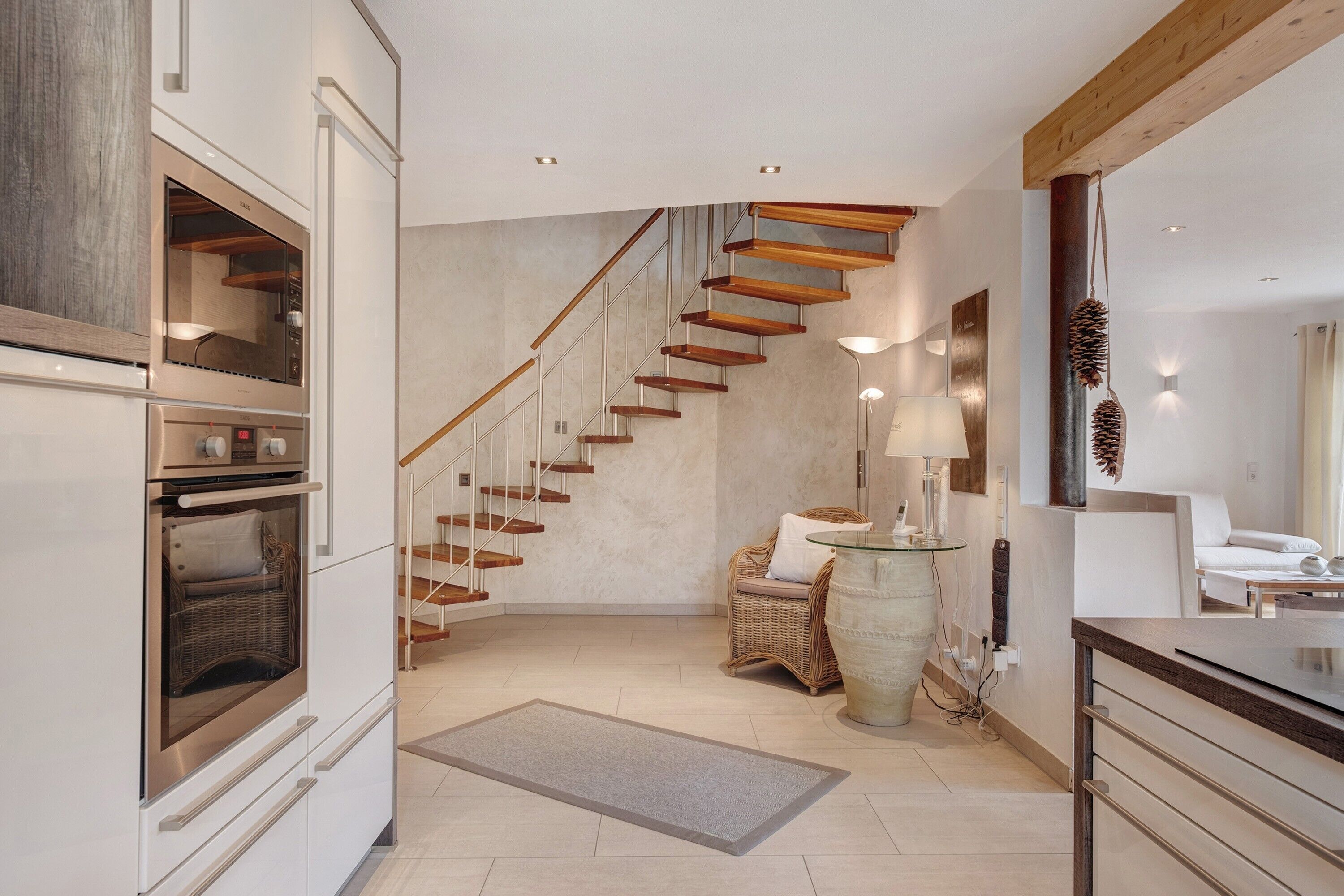 A modern kitchen with built-in appliances, a wooden staircase, wicker furniture, and a large vase.
