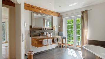 A modern bathroom with a large mirror, wooden vanity, and a bathtub.