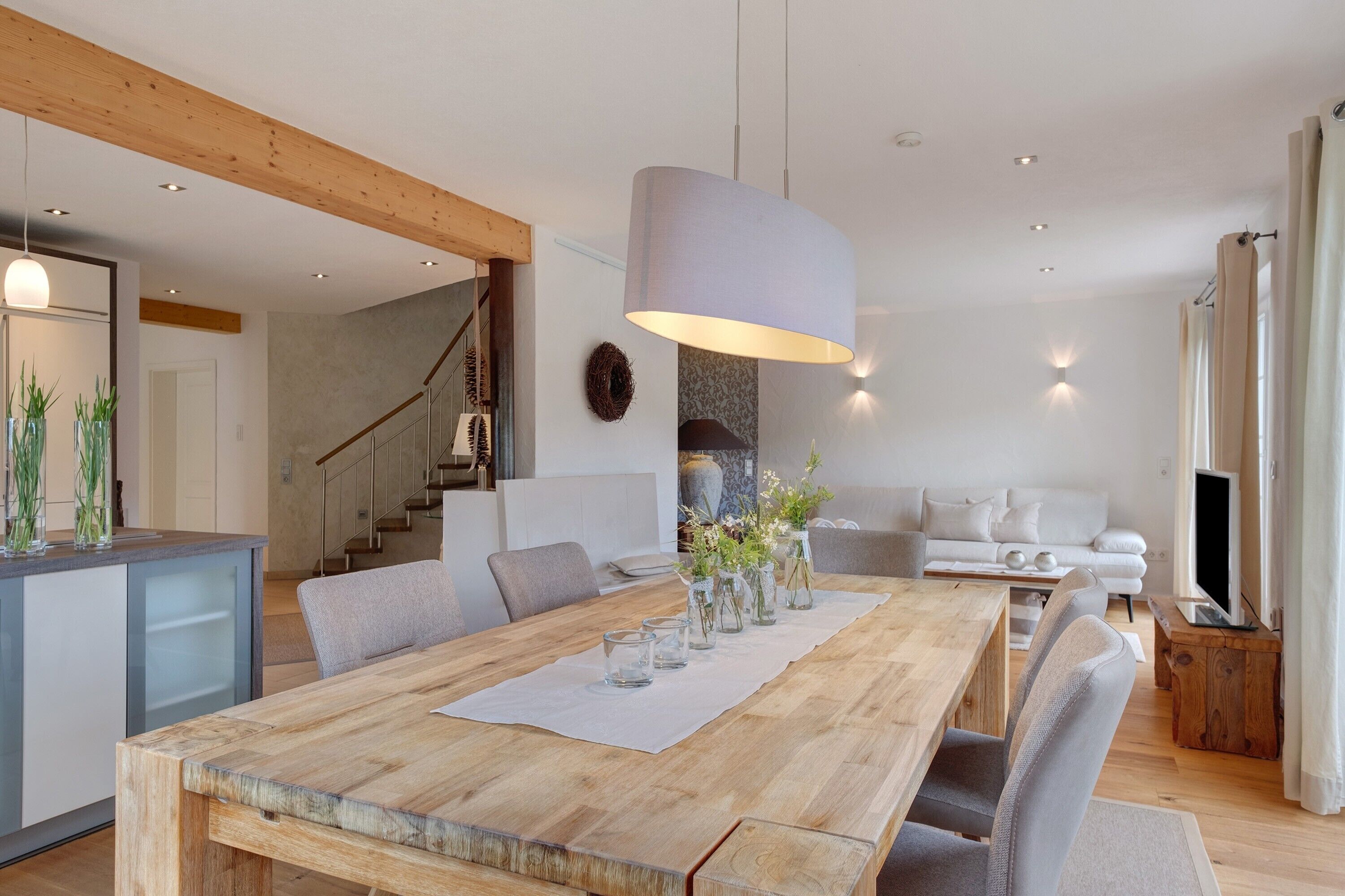 Un salón moderno con una mesa de comedor de madera, un sofá gris y una escalera que lleva a otro nivel.
