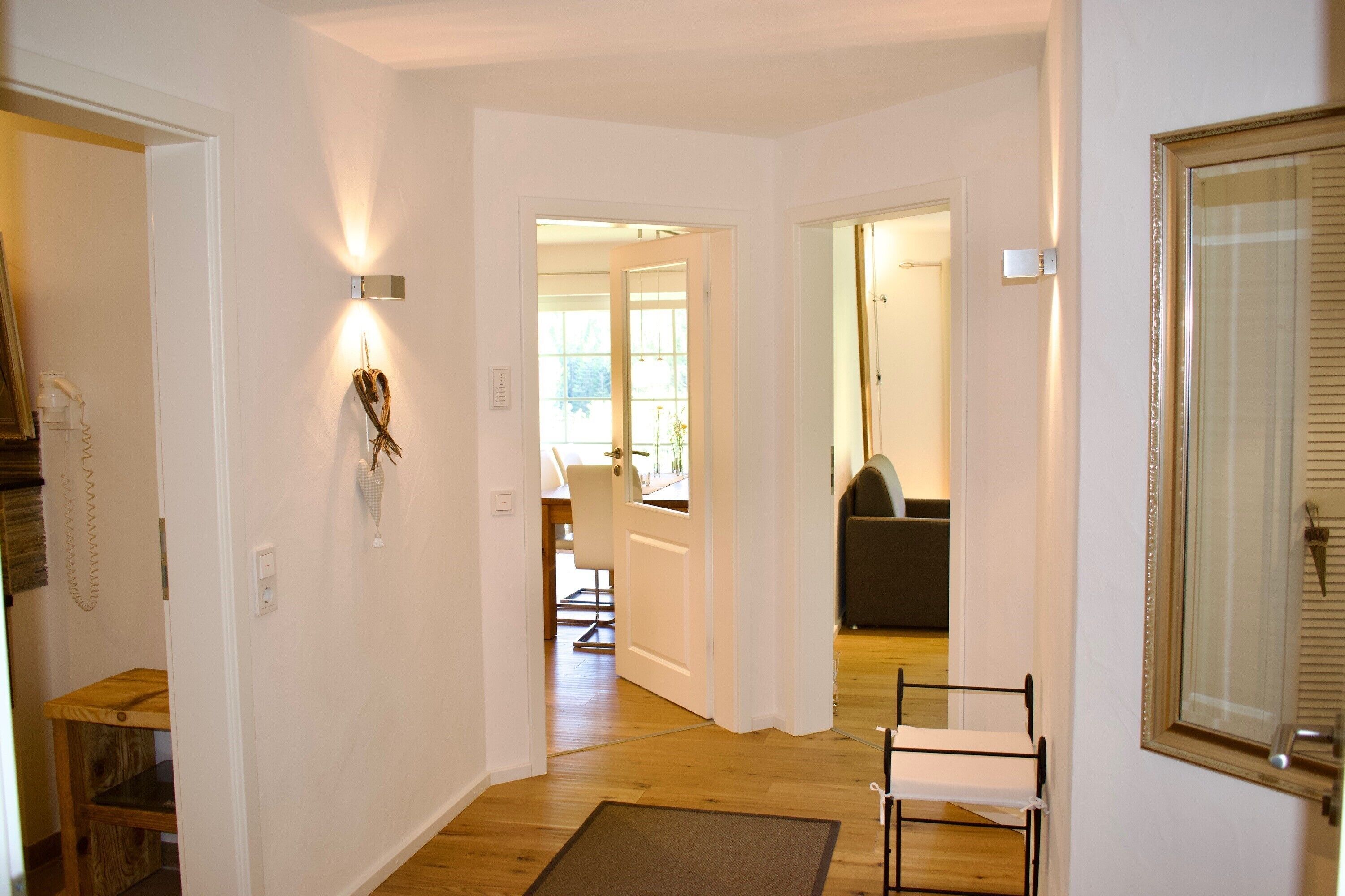 A hallway with a wooden floor, a white door, and a framed mirror on the right.