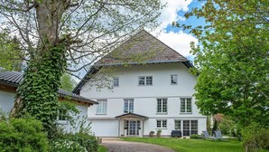 A two-story house with a white exterior, a tiled roof, and a gravel driveway leading to a front door. - Apartment '2 Natursuite' with Valley View, Shared Garden, Sauna and Wi-Fi (Furtwangen im Schwarzwald)