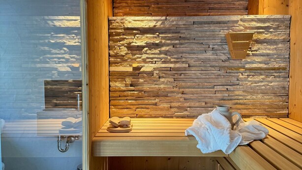 A sauna with wooden benches, a stone wall, and a glass door leading to a shower area.