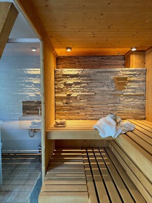 Una sauna con bancos de madera, pared de piedra y puerta de vidrio que da a una zona de ducha.