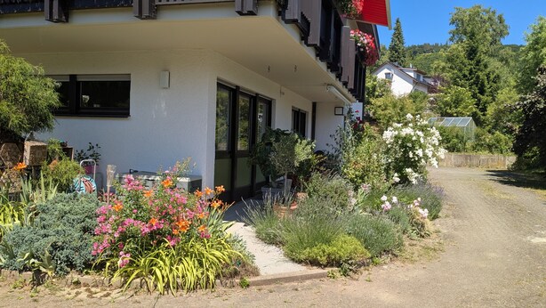 Ein Gebäude mit heller Fassade, großen Fenstern und einem Balkon mit roten Geländern.