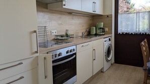 Eine kompakte Küche mit Einbauofen, Waschmaschine und Kaffeemaschine.