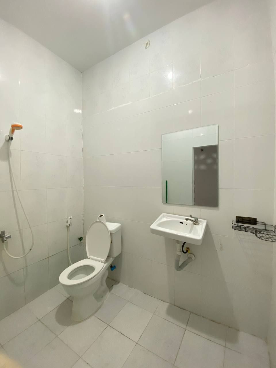 A small, clean bathroom with white tiles, a toilet, a sink, and a shower.