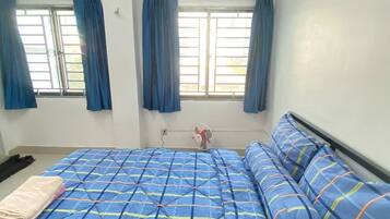 Un dormitorio con una cama grande, dos ventanas con cortinas, un ventilador de techo y una mesita de noche.