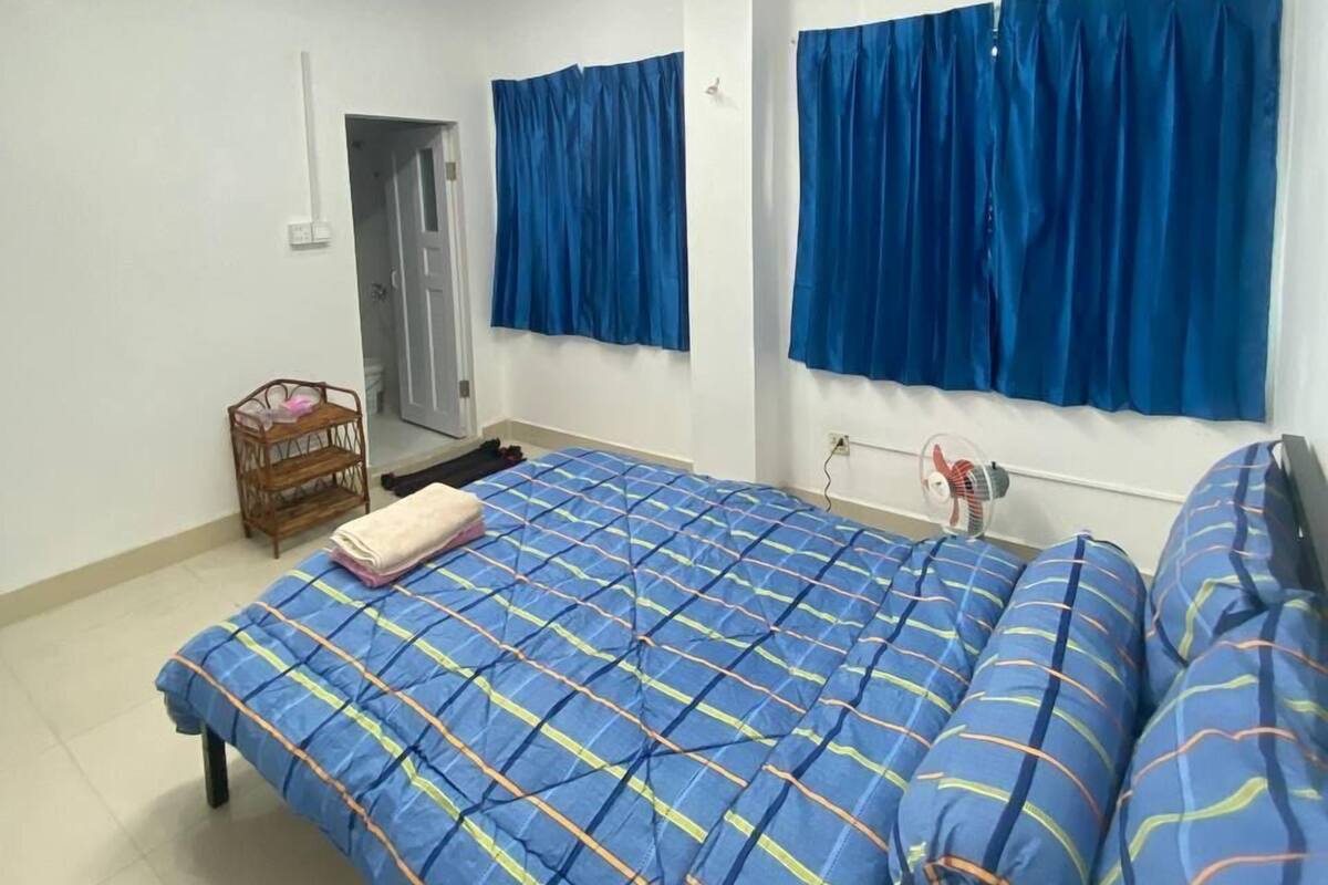 A bedroom with a bed, a fan, a window with blue curtains, and a door.