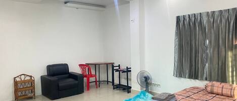 A modern room with a bed, a chair, a small table, a fan, and a window with curtains.
