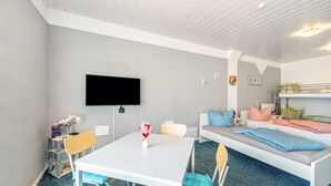 Una habitación moderna con una mesa blanca, un sofá, una cama litera, un televisor de pantalla plana y un escritorio pequeño con una silla.