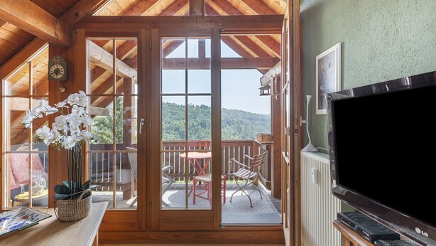 A wooden-framed room with a sliding glass door leading to an outdoor patio with a table and chairs.