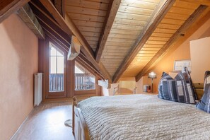 Une chambre avec un plafond en bois, un lit recouvert d’une courtepointe, une fenêtre donnant sur un beau paysage et un radiateur.