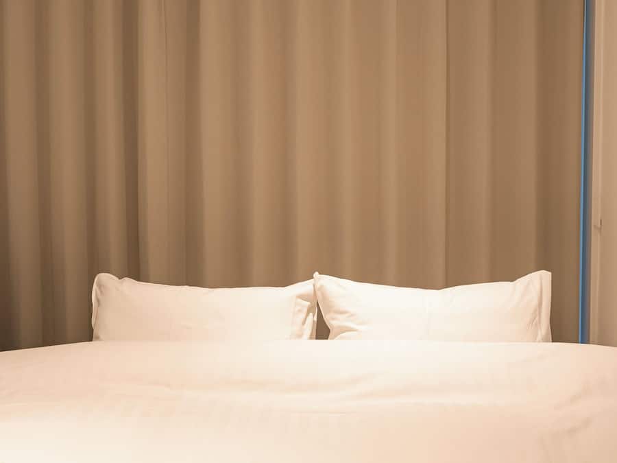 A bed with white bedding and a beige curtain backdrop.