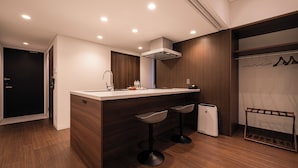 A modern kitchen with a central island, bar stools, a built-in oven, and a wooden wardrobe with hanging space.