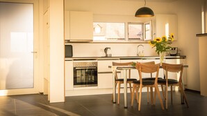 A modern kitchen with a dining area, including a stove, oven, and a table with chairs. - Apartment 'Südgarten' with Vineyard View, Private Terrace and Wi-Fi (Vogtsburg im Kaiserstuhl)