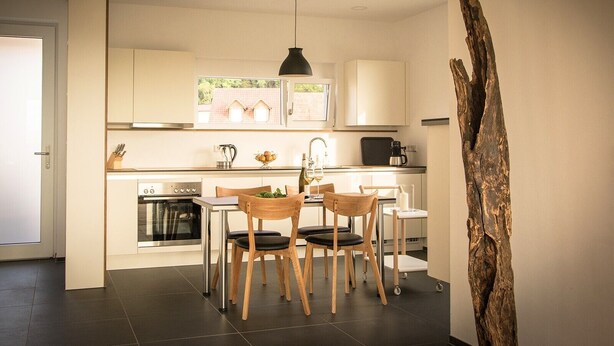 Een moderne keuken met een eethoek, een koffieapparaat en uitzicht op huizen door het raam.