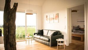 Een moderne woonkamer met een leren bank, een houten vloer en een groot raam met uitzicht op een wijngaard.