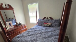 Une chambre à coucher avec un lit à baldaquin, une commode, un miroir et une fenêtre avec des stores.