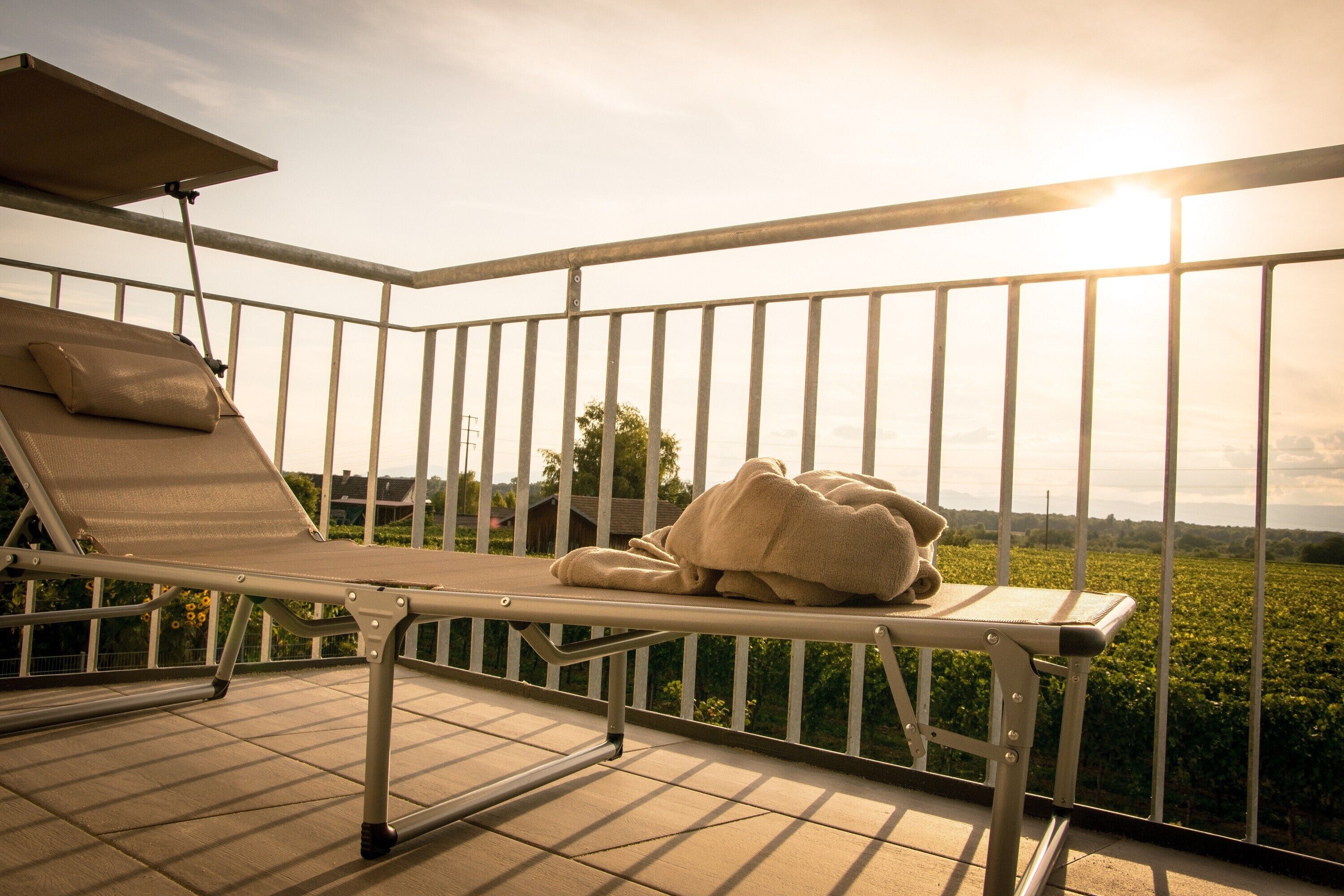 Ein Balkon mit Liegestuhl und Handtuch, mit Blick auf einen Weinberg.