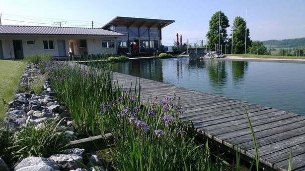 A lakeside property with a wooden dock, a building with a covered patio, and a view of the lake. - Apartment 'Roth' with Terrace and Wi-Fi (Frickingen)