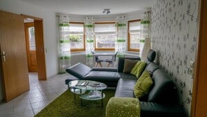 A modern living room with a sofa, a glass coffee table, and a view through large windows. - Apartment 'Roth' with Terrace and Wi-Fi (Frickingen)