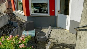 A small outdoor seating area with a table and chairs, a window with a view, and a door. - Apartment 'Roth' with Terrace and Wi-Fi (Frickingen)