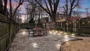 A backyard with a patio table and chairs, surrounded by a wooden fence and trees. - Charming 3-bedroom house in wonderful St. Louis with AC, WiFi (St. Louis)