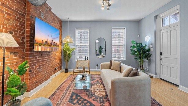 A living room with a brick wall, a sofa, a coffee table, and a large painting. - Charming 3-bedroom house in wonderful St. Louis with AC, WiFi (St. Louis)