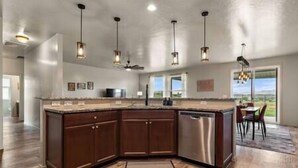 A modern kitchen with a large island, pendant lighting, and a view of the outdoors. - Private 7-Acre Wine Trail Estate near Lake Lowell (Caldwell)