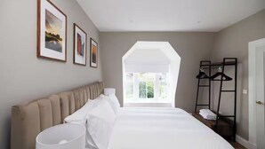 Un dormitorio con una cama grande, un radiador, una ventana con vistas y un perchero.