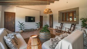 A spacious living area with a high ceiling, a large TV mounted on the wall, a rustic wooden rocking chair, and a unique planter in the center. - Can Cama Rotja, pool, barbecue & incredible views (Inca)
