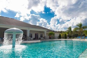Une piscine avec une fontaine, un patio couvert et un bâtiment doté d’un toit en pente.