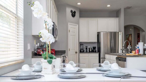Una cocina moderna con armarios blancos, electrodomésticos de acero inoxidable y un comedor listo para una comida.