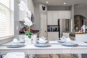 A modern kitchen with white cabinets, stainless steel appliances, and a dining area set for a meal. - Stylish Family Retreat in Kissimmee (Kissimmee)